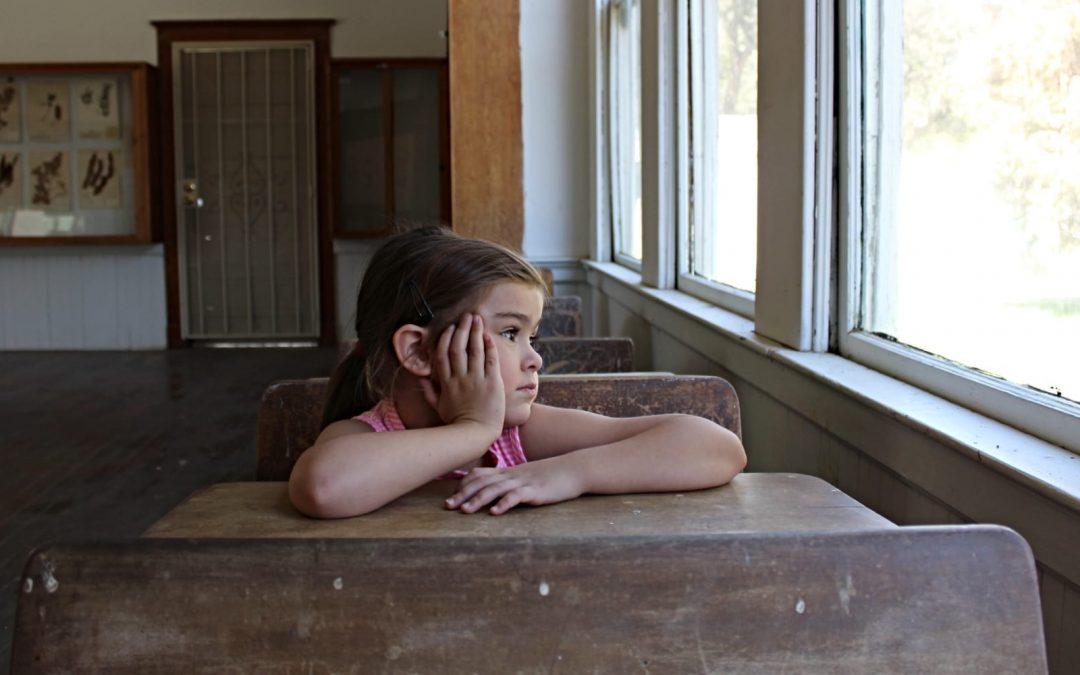 A young girl sitting at a school desk looking out the window