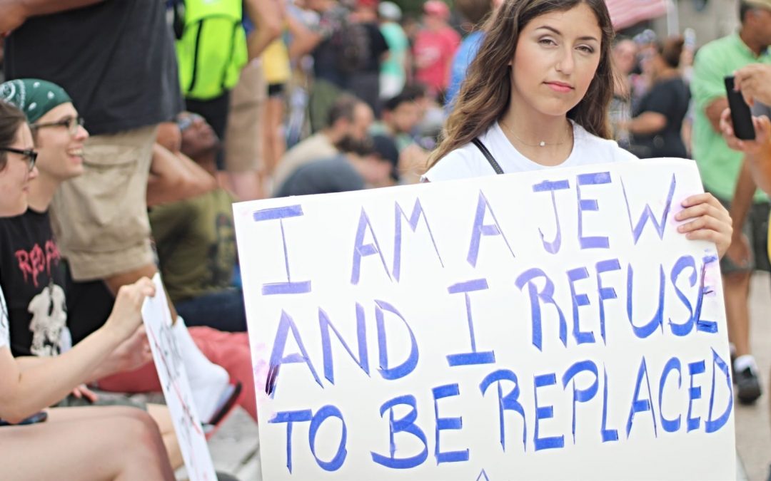 A woman holding a sign that says I am a Jew and I refuse to be replaced