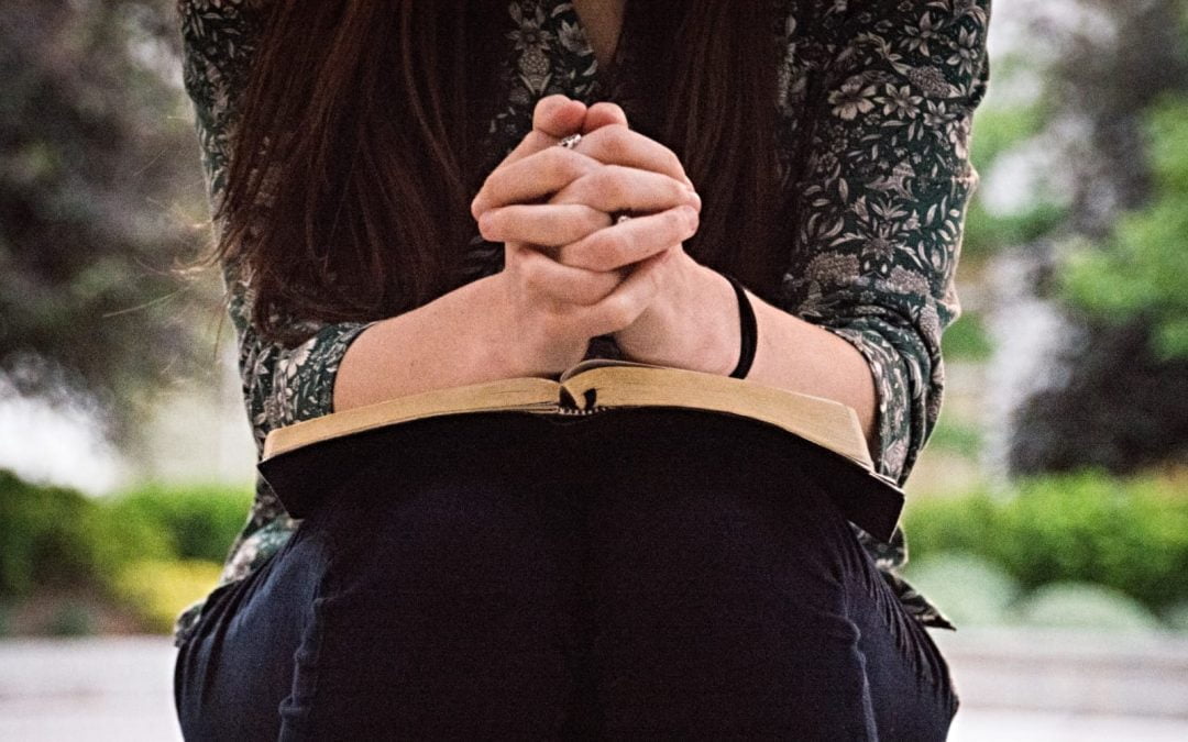 Woman with hands folded on Bible in prayer