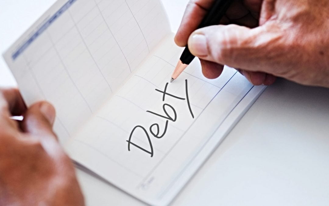 Person writing word ‘debt’ in banking book