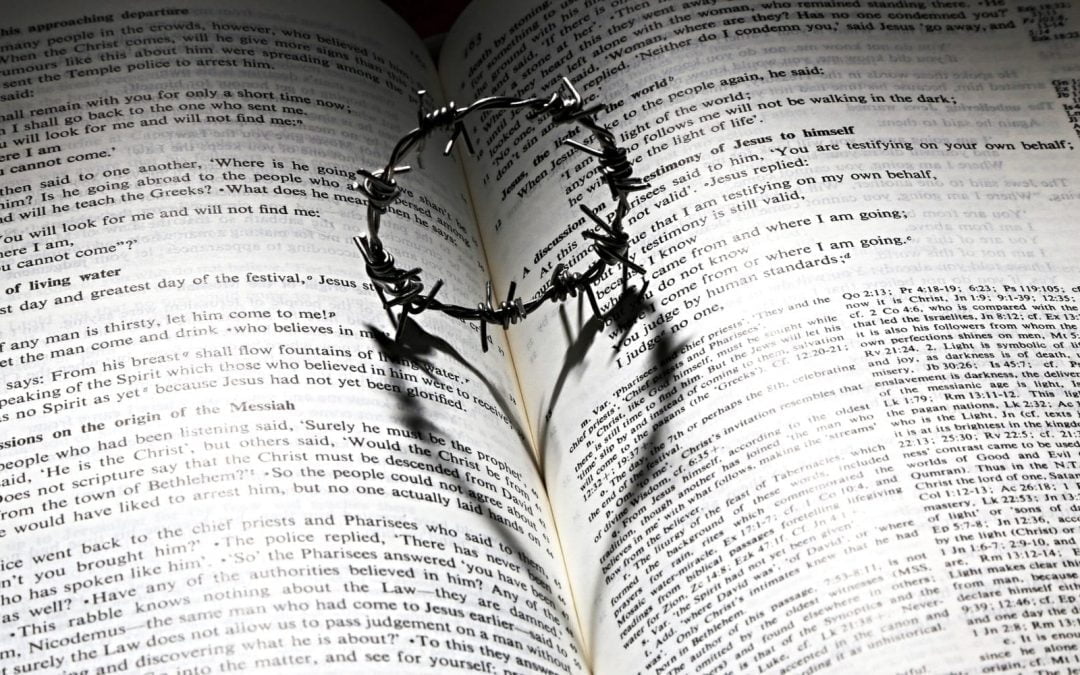 Barbed-wire ring casting heart shadow on Bible pages