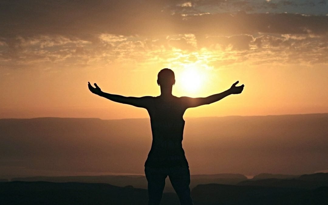 Silhouetted woman expressing gratefulness at sunrise