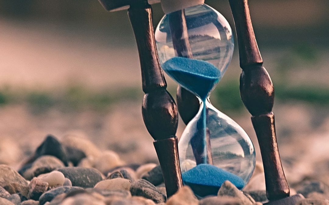 Hourglass with blue sand resting in rocks