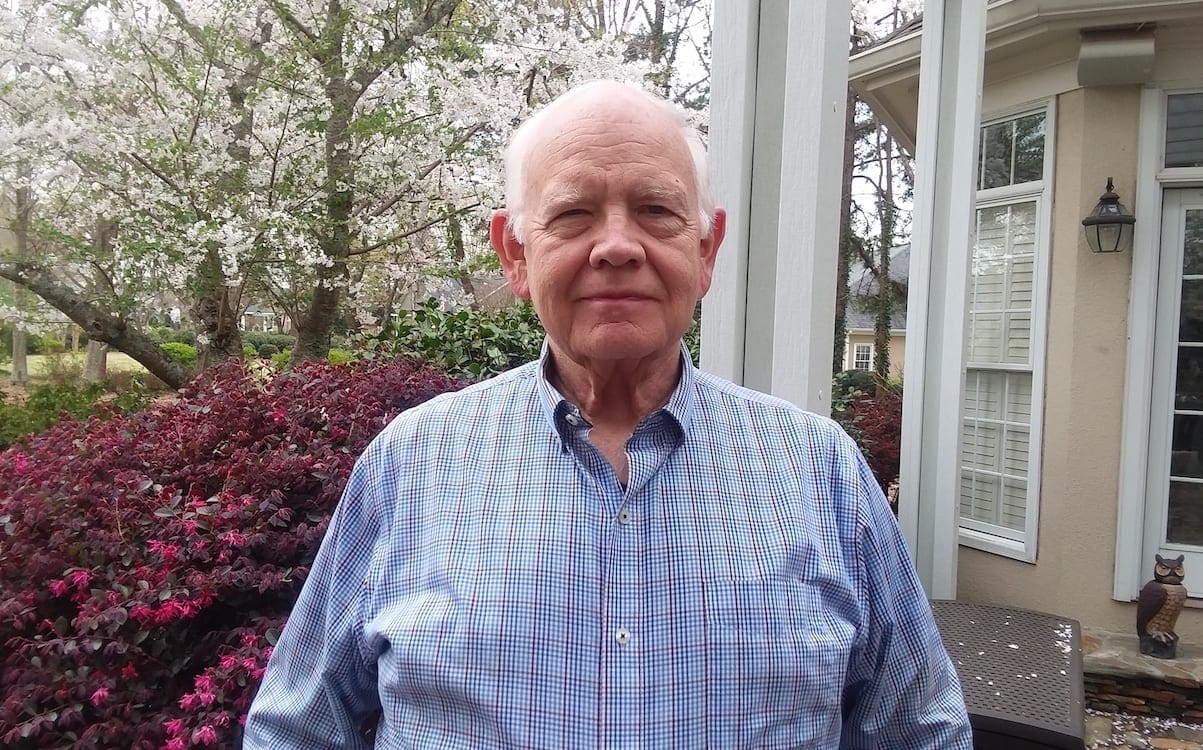 A man standing in front of a house and bushes.